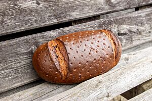 Das dunkelbraun ausgebackene Roggenmischbrot hat eine stark glänzende, gestippte Kruste mit quer gesetzten Einschnitten an beiden Enden.