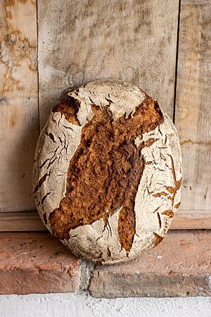 Ein ovaler Brotlaib lehnt aufrecht an einer rustikalen Holzwand.