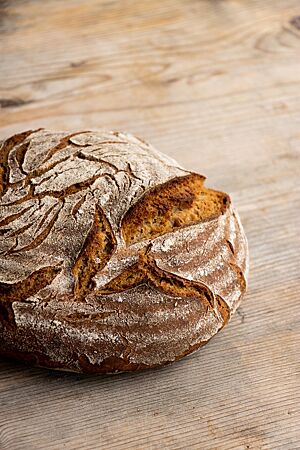 Ein rundes Roggenmischbrot mit bemehlter Kruste liegt auf einem Holztisch.