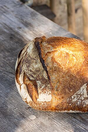 Das goldbraun ausgebackene Weizensauerteigbrot liegt auf einem rustikalen Holztisch.
