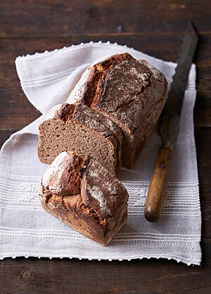 Der in der Kastenform kräftig ausgebackene Braunbär liegt angeschnitten auf einem weißen Tuch. Rechts neben dem Brot liegt ein rustikales Brotmesser.