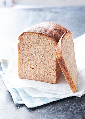 Eine Scheibe des Sandwich-Brotes lehnt seitlich am angeschnittenen Laib. Die fluffige, kleinporige Krume wird von einer feinen Kruste umgeben.
