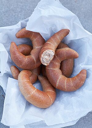 Die Hufeisen liegen in einem mit weißem Papier ausgelegten Drahtkorb. Ein auseinandergebrochenes Hufeisen zeigt die wattige, kleinporige Krume die von einer feinen, hellbraunen Kruste umgeben wird.