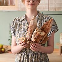 Eine Studentin hält drei Baguettestangen mit knuspriger Kruste und grobporiger Krume in den Händen.
