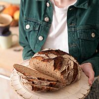 Ein Roggenmischbrot liegt mit mehreren abgeschnittenen Scheiben auf einem Holztablett. Die lockere, kleinporige Krume ist umgeben von einer rustikal aufgerissenen, kräftig ausgebackenen Kruste.
