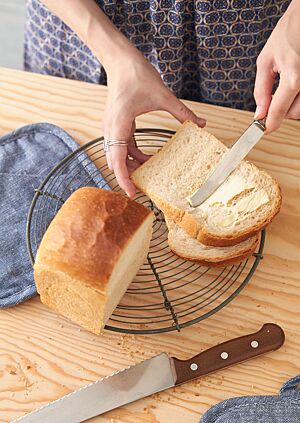 Eine Scheibe des goldbraun ausgebackenen Sandwichbrotes mit heller, fluffiger Krume wird mit Butter bestrichen.