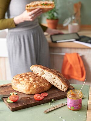 Auf einem Holzbrett liegt das angeschnittene Fladenbrot mit goldgelber Kruste und mittelporiger, lockerer Krume.