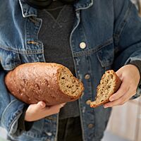 Ein abgebrochenes Stück des großen, dunkelbraun ausgebackenen Dinkelmischbrotes mit gestippter Oberfläche zeigt die klein- bis mittelporige, lockere Krume.