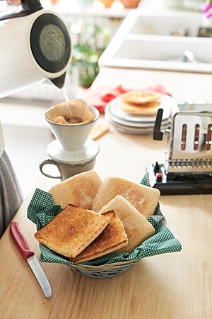 Drei flache, goldgelb ausbackene Toasties liegen neben zwei goldbraun getoasteten Hälften eines aufgeschnittenen Toasties in einer Schale.