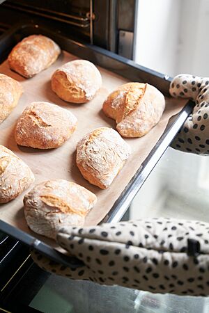 Ein Blech mit neun goldgelb ausgebackenen Weizenmischbrötchen wird aus dem Ofen geholt.