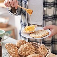 Auf ein halbiertes Dinkel-Haferbrötchen wird Honig geträufelt. Die goldbraun ausgebackenen, mit Haferflocken bestreuten Crispy Oats haben eine lockere, mittelporige Krume.