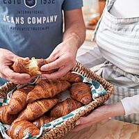 In einem Flechtkorb liegen mehrere goldbraun ausgebackene, glänzende Croissants. Eines davon wird auseinandergezogen und lässt die wattige, sehr elastische Krume erkennen.