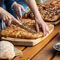 Drei Focaccias liegen nebeneinander auf Holzbrettern und werden in kleine Stücke geschnitten.