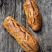 Zwei kräftig ausgebackene Kartoffelseelen mit leicht aufgerissener Kruste liegen auf einem rustikalen Holztisch.