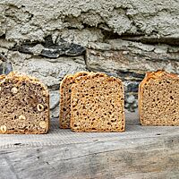 Neben dem Dinkel-Hirse-Kasten (rechts) stehen ein Dinkel-Hirse-Karotten-Brot (Mitte) und ein Dinkel-Hirse-Nuss-Brot (links).