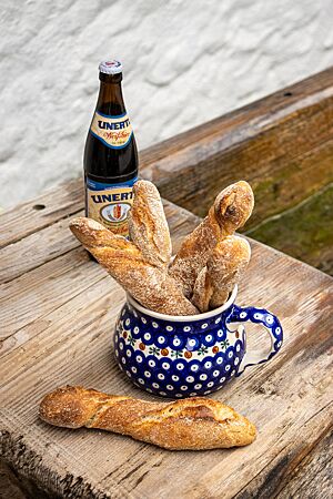 In einem blau-weiß gemusterten Krug stehen vier kräftig ausgebackene Haager Bierstangen neben einer Flasche Weißbier.
