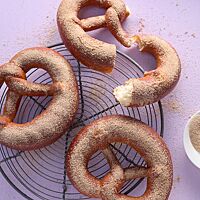 Drei Soft Pretzels mit Zimtzucker auf der weichen, goldbraun ausgebackenen Kruste liegen auf einem runden Abkühlgitter. Eine auseinandergebrochene Pretzel zeigt die helle, wattige Krume.