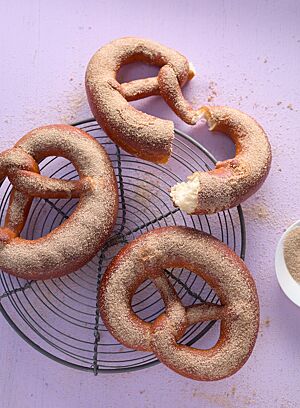 Drei Soft Pretzels mit Zimtzucker auf der weichen, goldbraun ausgebackenen Kruste liegen auf einem runden Abkühlgitter. Eine auseinandergebrochene Pretzel zeigt die helle, wattige Krume.