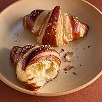 Ein auseinandergebrochenes und ein ganzes Laugencroissant liegen in einem tiefen Teller. Die Krume der Croissants ist wattig und sehr elastisch, die Kruste ist fein und goldbraun ausgebacken.